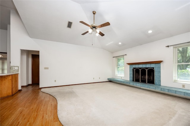 unfurnished living room with light hardwood / wood-style flooring, vaulted ceiling, a tiled fireplace, and ceiling fan