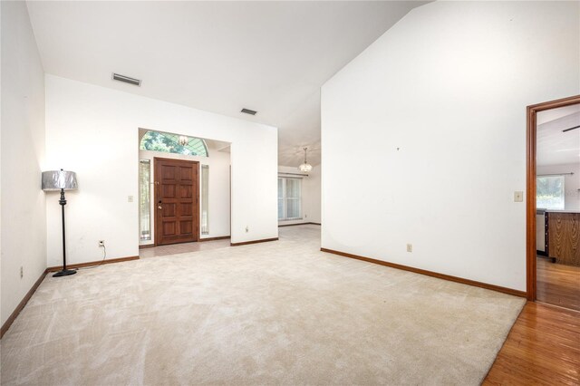 unfurnished living room with vaulted ceiling, an inviting chandelier, and light hardwood / wood-style floors