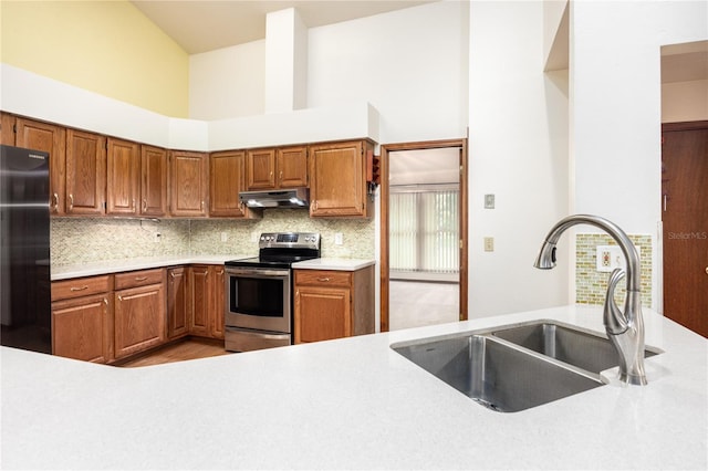 kitchen featuring light wood-type flooring, stainless steel electric range, backsplash, sink, and black fridge