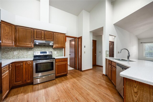 kitchen featuring light wood-type flooring, high vaulted ceiling, tasteful backsplash, stainless steel appliances, and sink