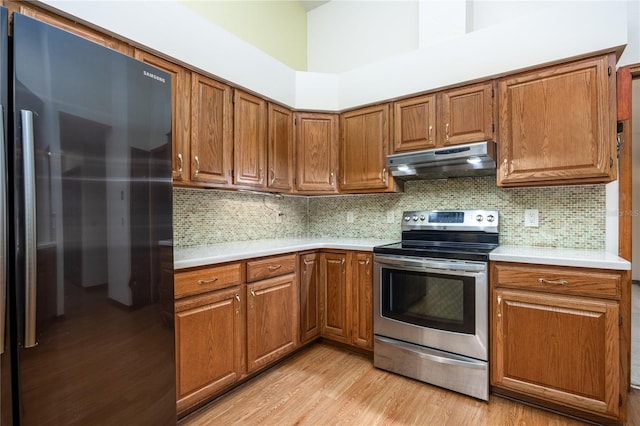 kitchen featuring stainless steel range with electric cooktop, light hardwood / wood-style flooring, decorative backsplash, and black fridge