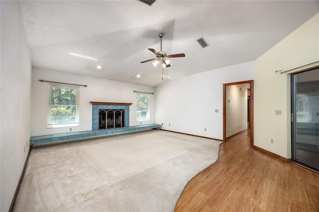 unfurnished living room featuring plenty of natural light, ceiling fan, a tiled fireplace, and wood-type flooring