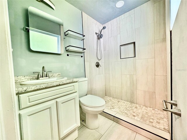 bathroom with tiled shower, vanity, toilet, and tile patterned floors