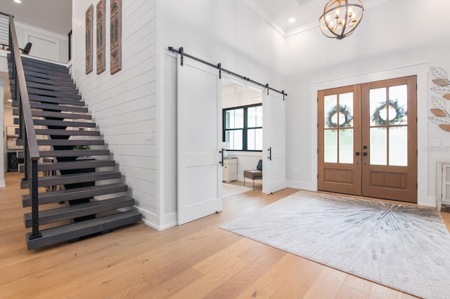 foyer entrance with light hardwood / wood-style floors, a chandelier, french doors, and a barn door