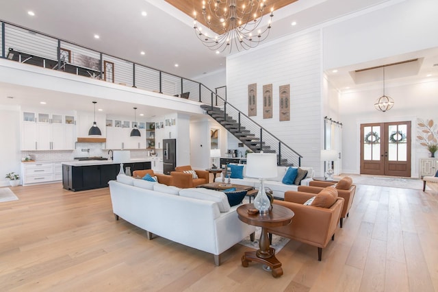 living room featuring light hardwood / wood-style floors, a towering ceiling, a notable chandelier, and french doors