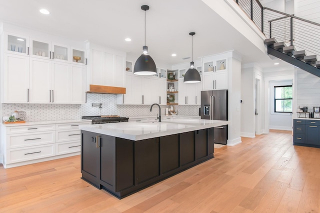 kitchen featuring range, high end fridge, white cabinets, light hardwood / wood-style flooring, and a center island with sink