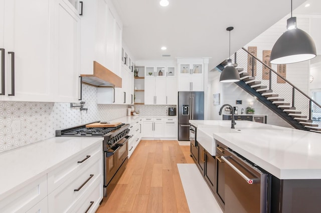 kitchen featuring premium range hood, white cabinetry, high end appliances, pendant lighting, and an island with sink