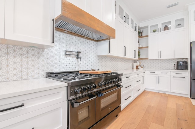 kitchen featuring double oven range, white cabinets, and custom range hood