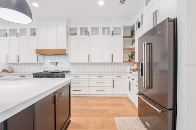 kitchen featuring light stone countertops, high quality fridge, range, white cabinetry, and light hardwood / wood-style floors