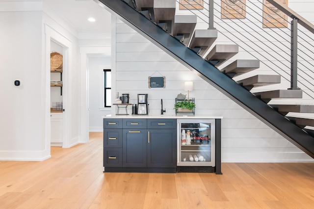 bar featuring crown molding, light hardwood / wood-style flooring, wine cooler, and blue cabinets