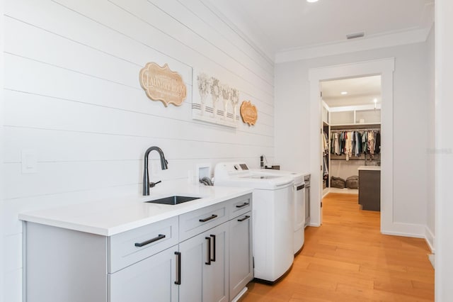 washroom with crown molding, sink, light wood-type flooring, washing machine and dryer, and cabinets