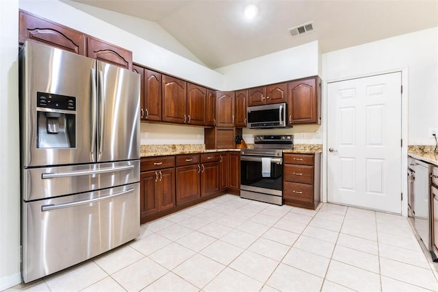 kitchen with light stone countertops, stainless steel appliances, vaulted ceiling, and light tile patterned flooring