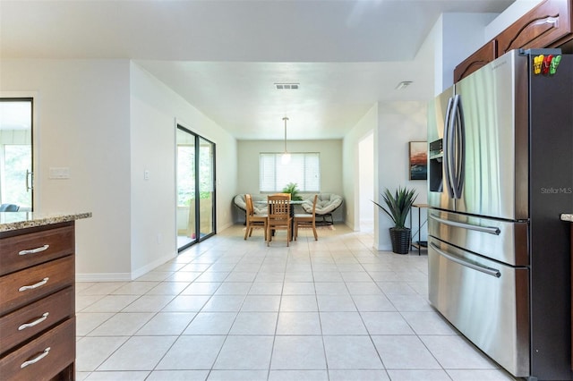 kitchen featuring stainless steel fridge, light tile patterned floors, light stone counters, and decorative light fixtures