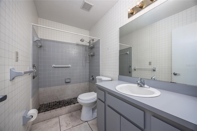 bathroom with vanity, a tile shower, tile walls, toilet, and tile patterned floors