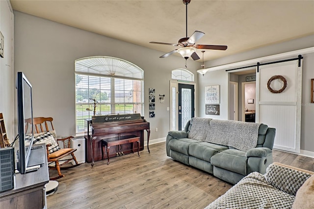 living room with light wood finished floors, ceiling fan, a barn door, and baseboards