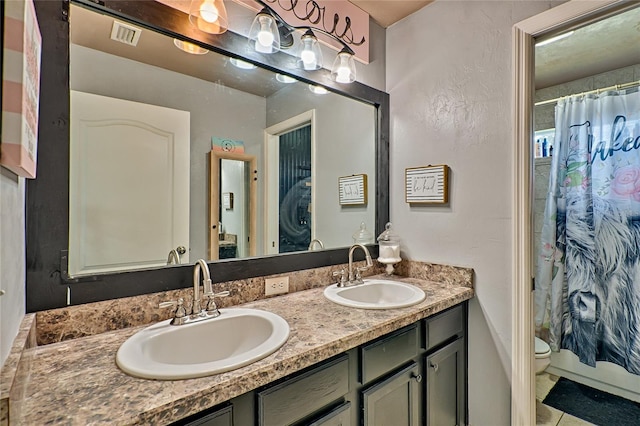 full bath featuring toilet, double vanity, visible vents, and a sink