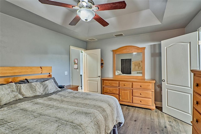 bedroom with light wood-type flooring, visible vents, and a raised ceiling