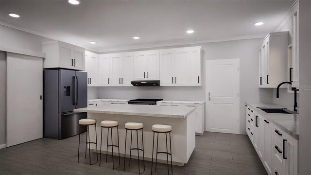 kitchen featuring a breakfast bar area, stainless steel refrigerator with ice dispenser, a center island, sink, and white cabinets