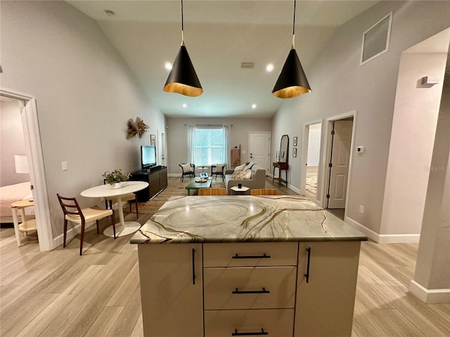 kitchen featuring light stone countertops, light wood-type flooring, a kitchen island, hanging light fixtures, and high vaulted ceiling