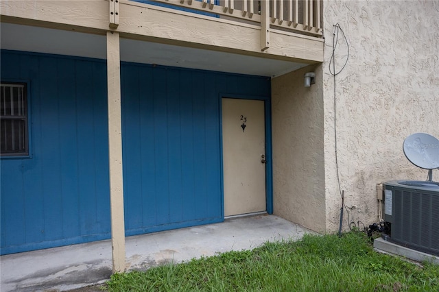 property entrance with stucco siding, cooling unit, and a balcony