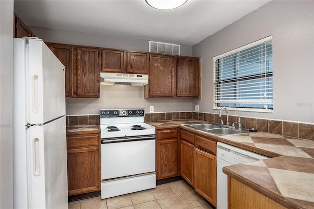 kitchen with visible vents, under cabinet range hood, light tile patterned floors, white appliances, and a sink