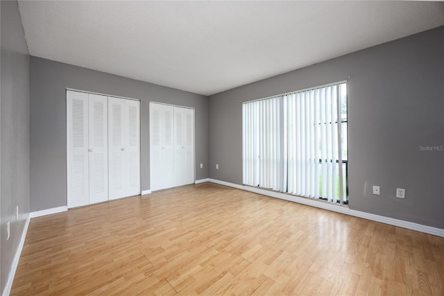 unfurnished bedroom with a textured ceiling, light hardwood / wood-style flooring, and two closets