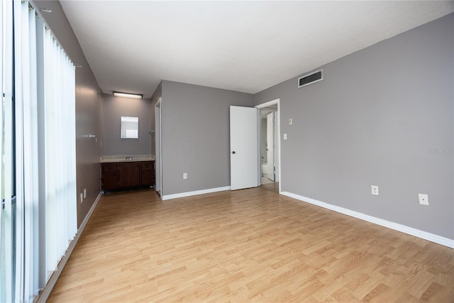 unfurnished bedroom featuring ensuite bath, baseboards, visible vents, and light wood-type flooring