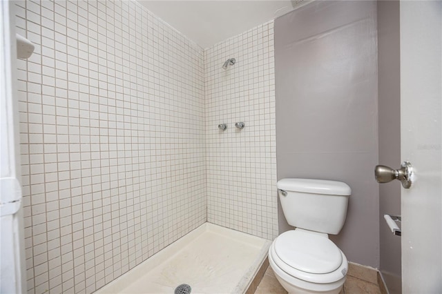 bathroom with tiled shower, toilet, and tile patterned flooring