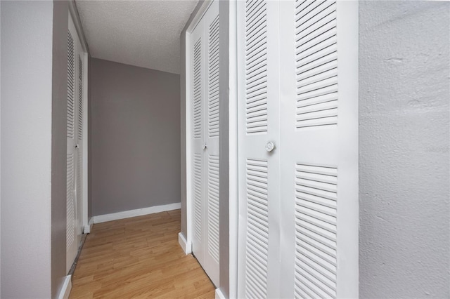 hall with baseboards, light wood-style floors, and a textured ceiling