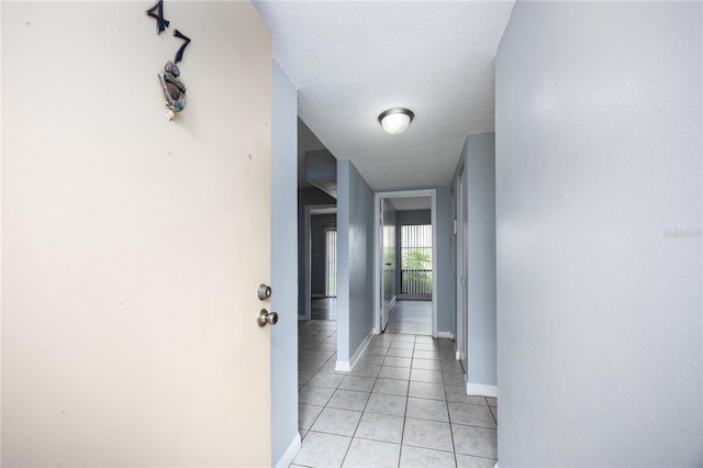 hall featuring light tile patterned flooring, baseboards, and a textured ceiling