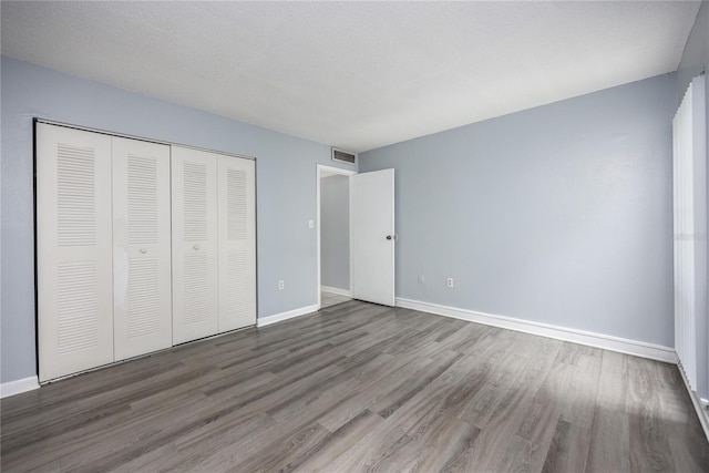 unfurnished bedroom with wood finished floors, visible vents, a closet, and baseboards