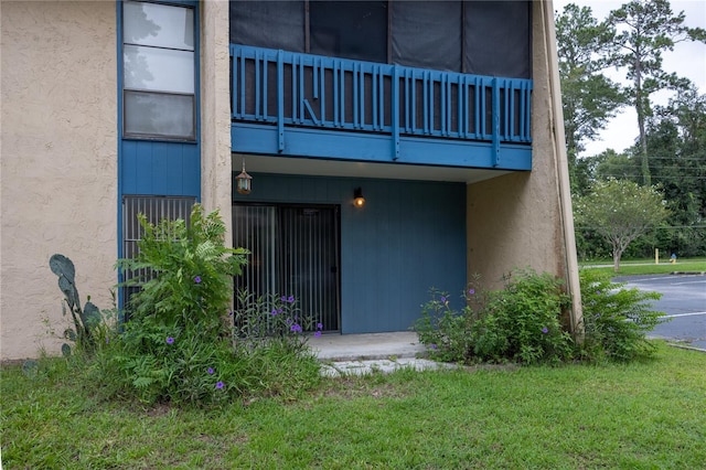 doorway to property featuring a balcony, a lawn, and stucco siding