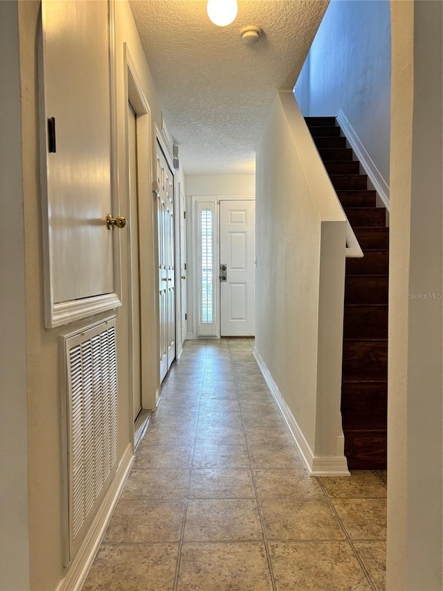 hallway with a textured ceiling and light tile patterned flooring