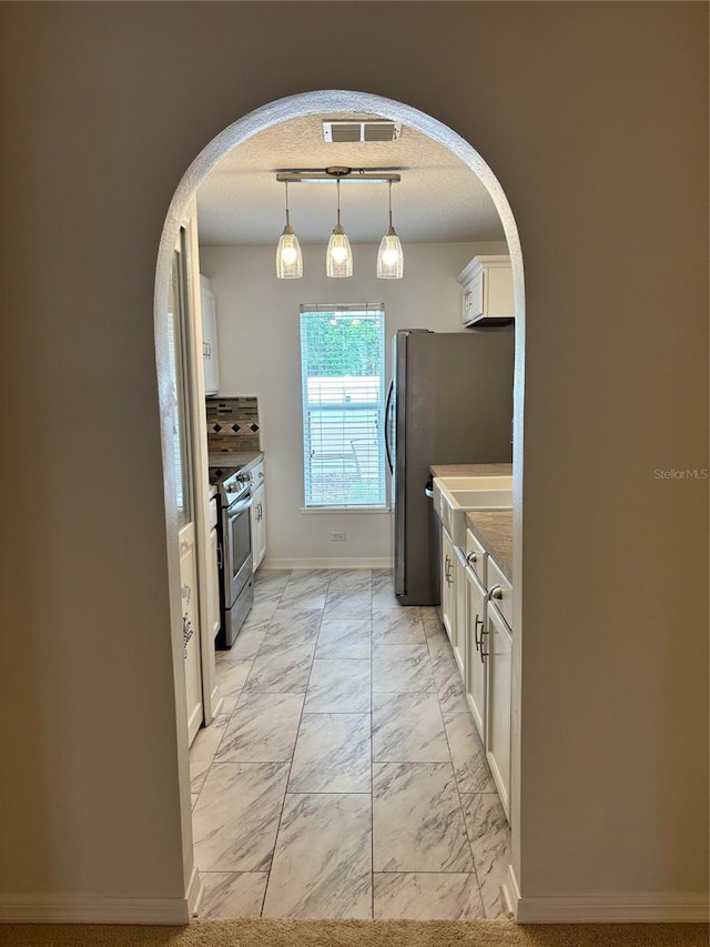 kitchen with white cabinets, hanging light fixtures, stainless steel appliances, and a textured ceiling