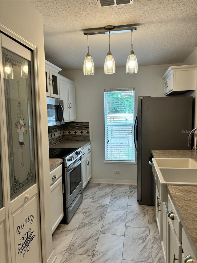 kitchen with tasteful backsplash, a textured ceiling, decorative light fixtures, appliances with stainless steel finishes, and white cabinets