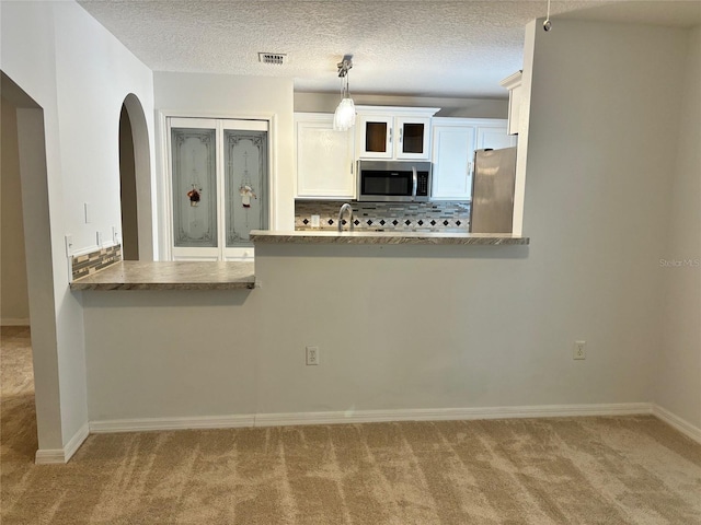 kitchen featuring light colored carpet, pendant lighting, appliances with stainless steel finishes, and white cabinetry