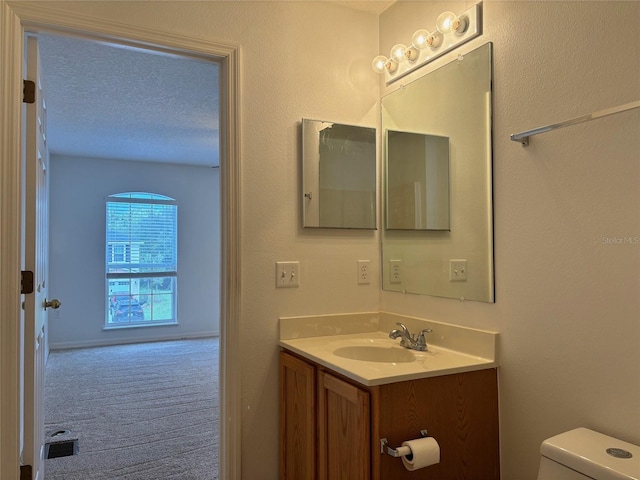 bathroom with a textured ceiling, vanity, and toilet