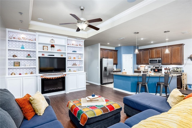 living room with sink, a tray ceiling, dark wood-type flooring, ceiling fan, and ornamental molding