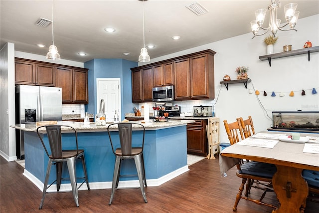 kitchen featuring a kitchen island with sink, decorative light fixtures, stainless steel appliances, and dark hardwood / wood-style floors