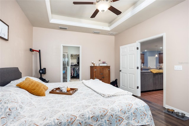 bedroom with dark hardwood / wood-style floors, a spacious closet, a closet, a tray ceiling, and ceiling fan