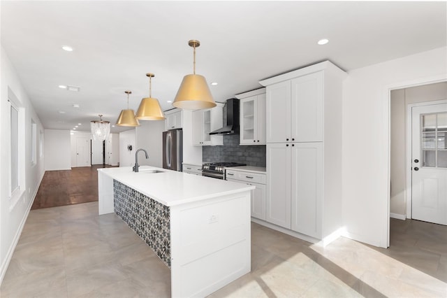 kitchen with stainless steel appliances, sink, wall chimney range hood, decorative light fixtures, and a center island with sink