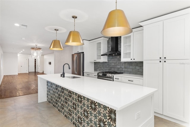 kitchen with wall chimney exhaust hood, a kitchen island with sink, appliances with stainless steel finishes, and light hardwood / wood-style flooring