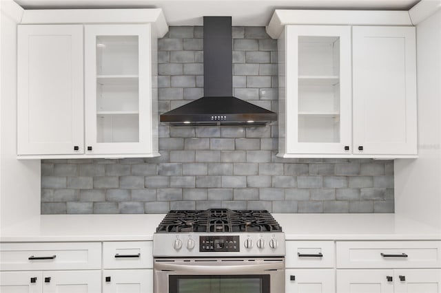 kitchen featuring decorative backsplash, white cabinetry, wall chimney range hood, and stainless steel gas range