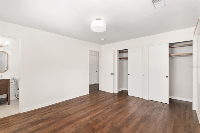 unfurnished bedroom with connected bathroom, multiple closets, and dark wood-type flooring