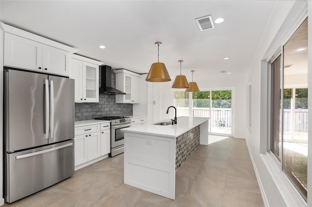 kitchen featuring white cabinets, sink, wall chimney exhaust hood, appliances with stainless steel finishes, and decorative light fixtures