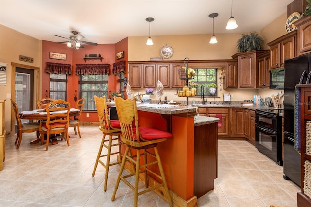 kitchen with pendant lighting, sink, a center island, a breakfast bar, and black appliances