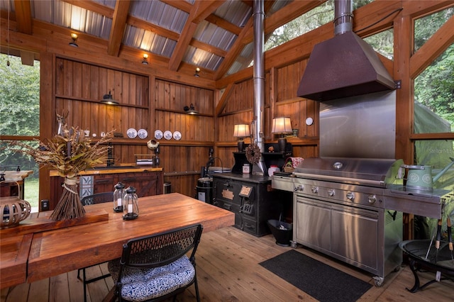 kitchen featuring light wood-type flooring, wooden walls, vaulted ceiling with beams, and custom range hood