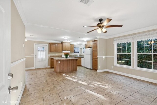 kitchen with light tile patterned flooring, a center island, white refrigerator, ornamental molding, and ceiling fan