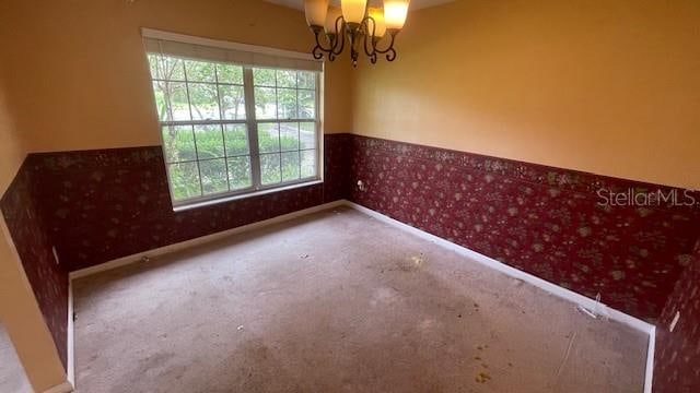 empty room with a wealth of natural light, carpet flooring, and a notable chandelier