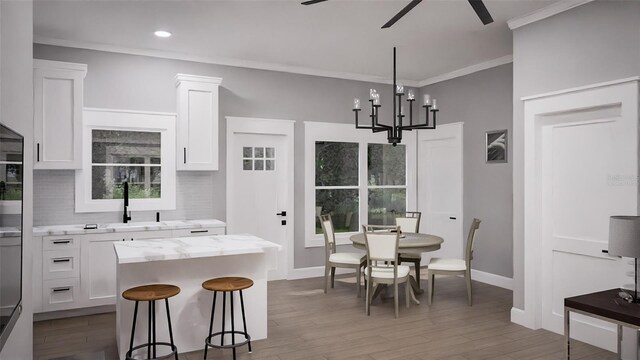 kitchen with ceiling fan with notable chandelier, white cabinets, a center island, and hardwood / wood-style floors